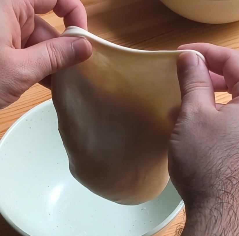 Masa de pizza estirada a mano mostrando el efecto velo o prueba de la ventana, con textura translúcida que indica buen desarrollo del gluten