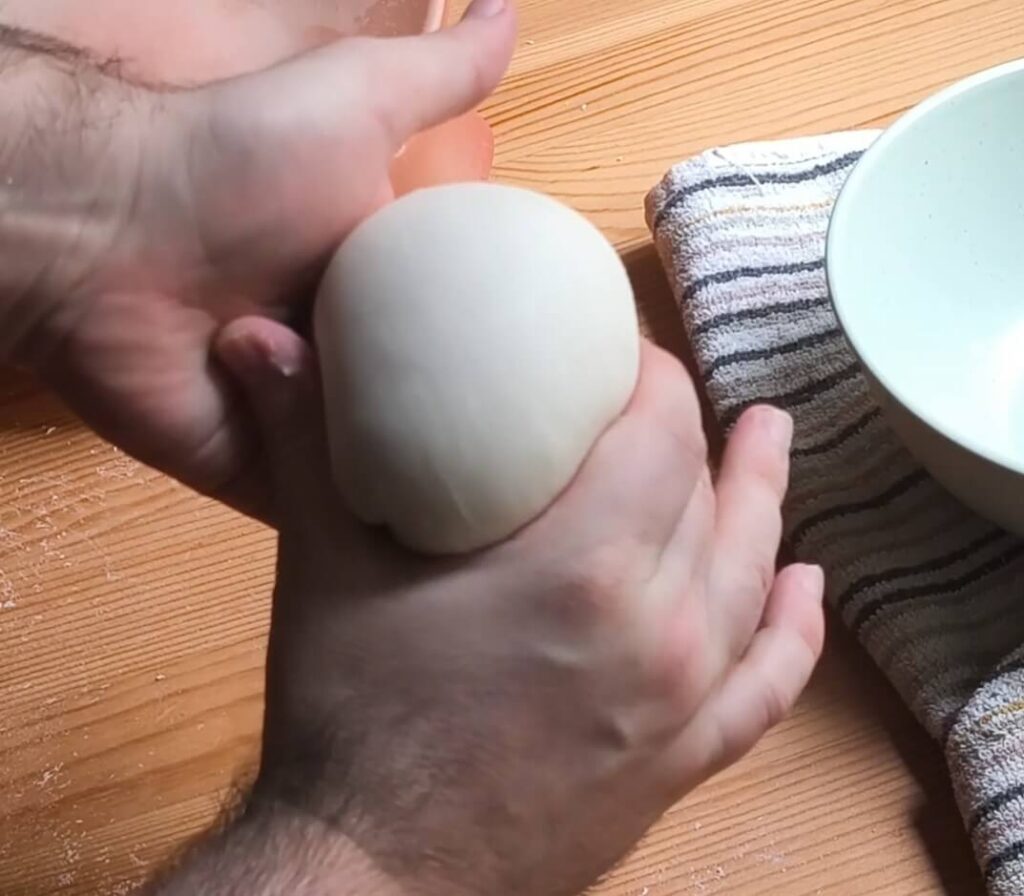 Boleado de masa de pizza a mano formando una bola lisa y tensa antes de la fermentación