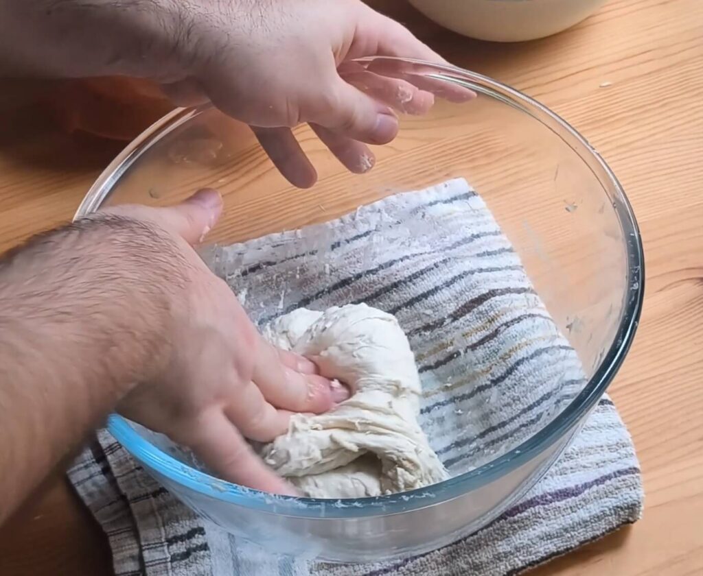 Masa de pizza pegajosa al inicio del amasado adherida a las manos y al bol antes de desarrollar el gluten