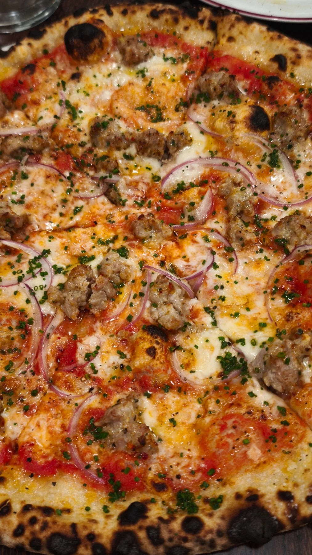 Detalle de una pizza con tomate, trozos de carne y cebolla morada